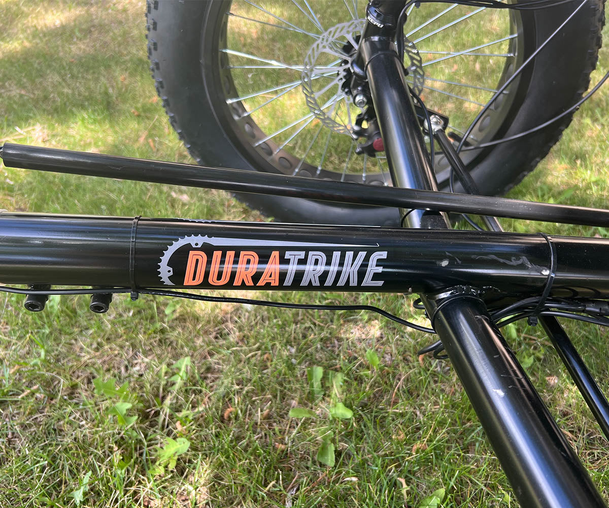 Close-up of the FX36e's tricycle's frame showing the "DuraTrike" logo and part of the front tire with grass background