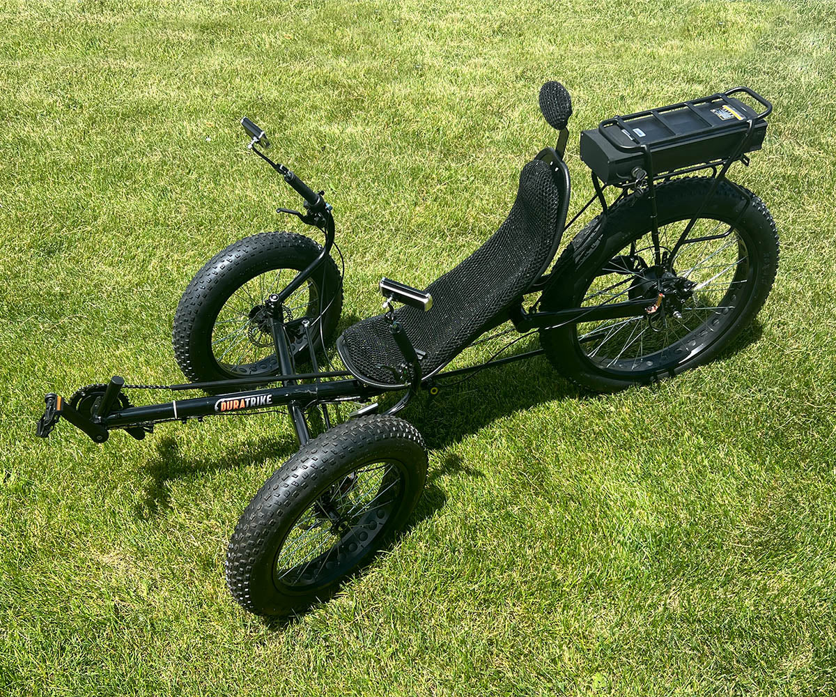DuraTrike FX36e on grass with black frame and fat tires. Front right angled view showing angled tires and mesh seat.