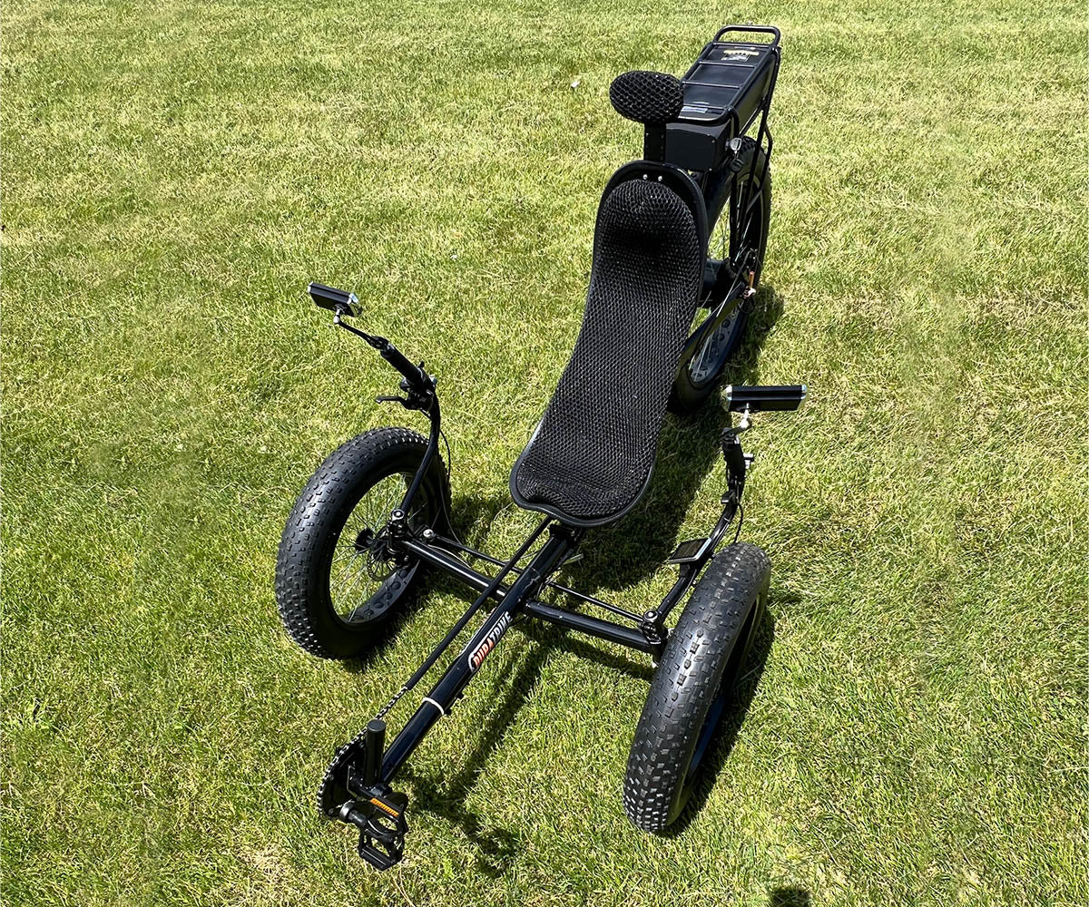 Top down view of FX36e recumbent trike on grass in sunlight with focus on front wheels and indirect steering assembly & handlebars