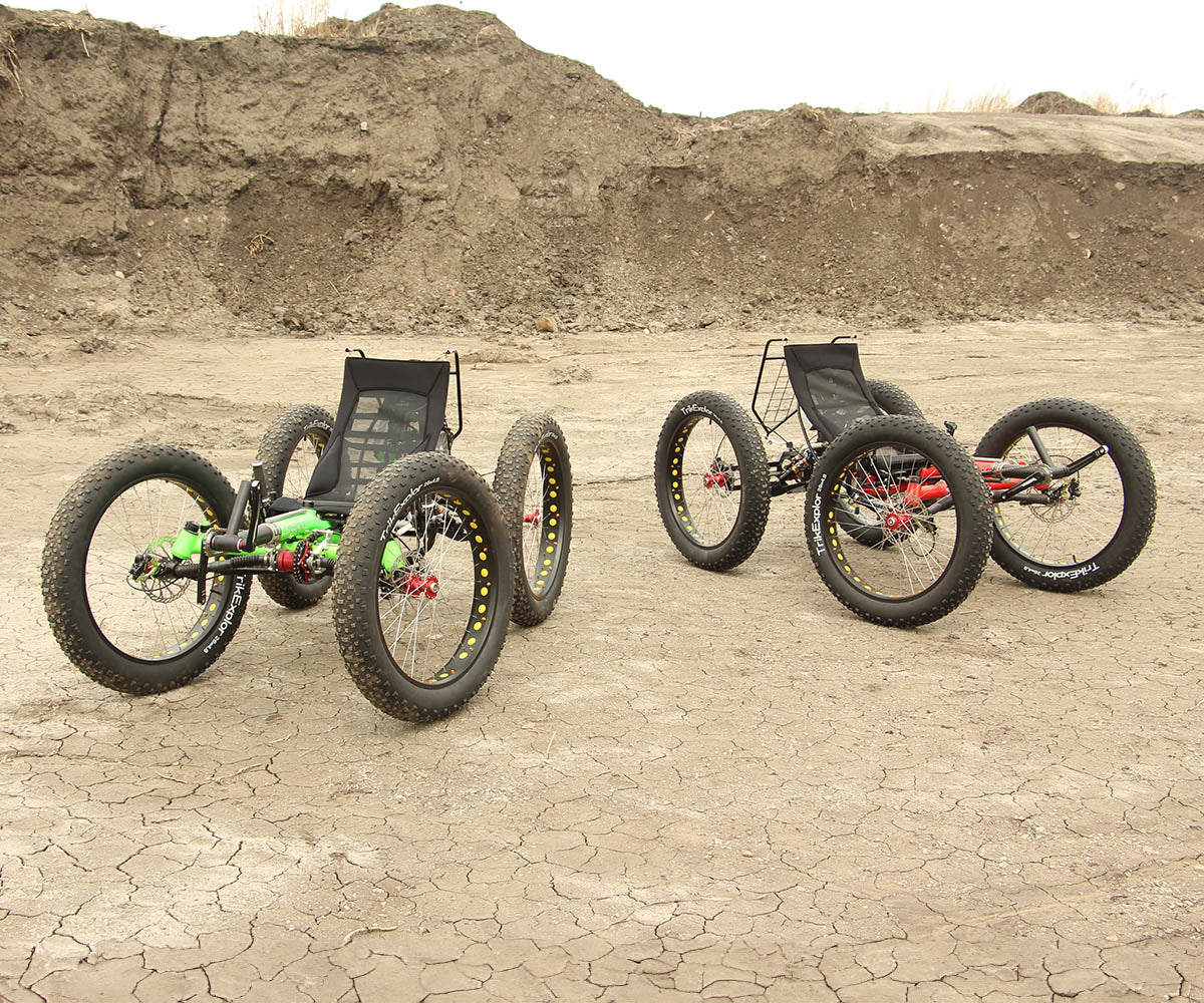 Two FT26e off-road recumbent trikes on cracked, dry ground, highlighting their robust tires and sturdy frames.