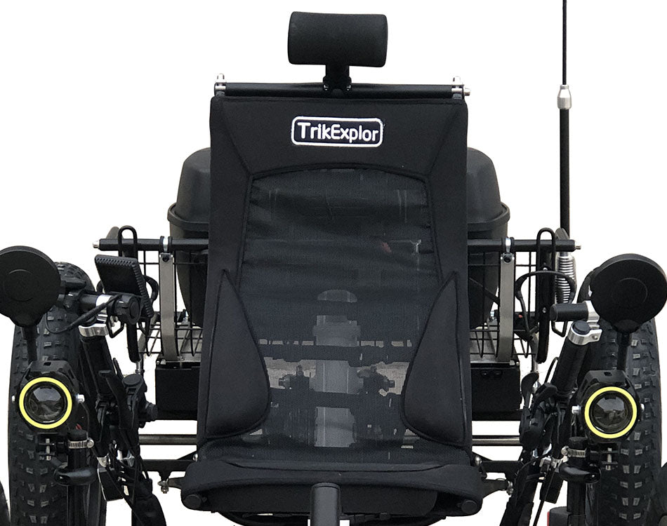 Close up of black mesh seat on a recumbent quad framed by headlights and off road tires. 