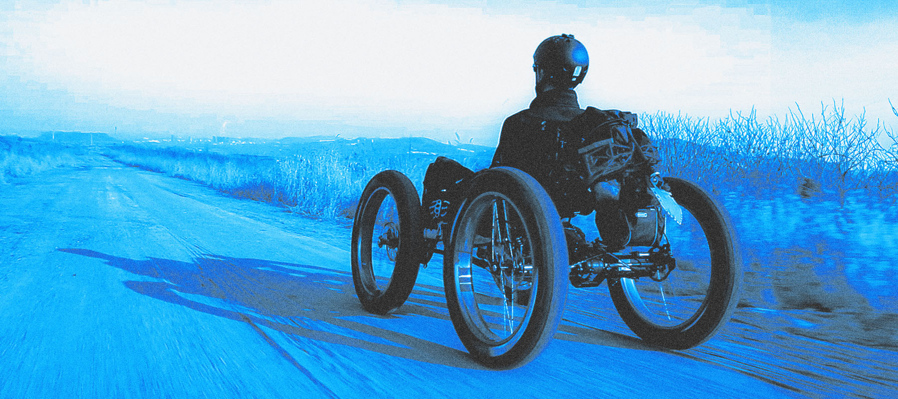 Blue hued image of person riding a quad bike on a scenic off-road trail at dusk.